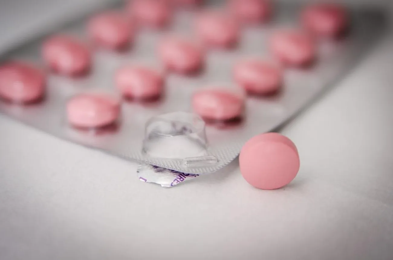 Farmacistă în halat alb la ghișeul unei farmacii de cartier, cu rafturi ordonate în spate
